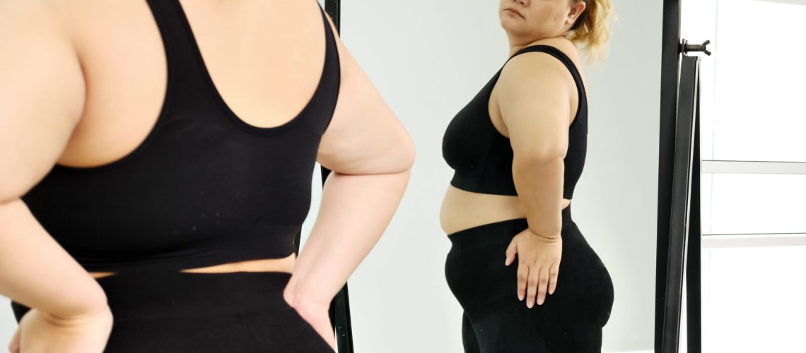 Chubby woman standing and looking at her stomach in a mirror.